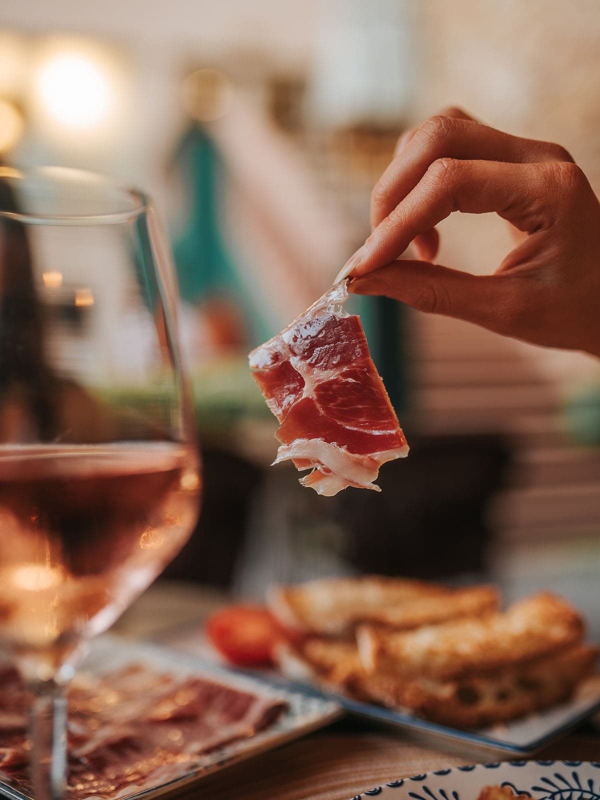 Mano sosteniendo una loncha de jamón ibérico junto a una copa de vino rosado