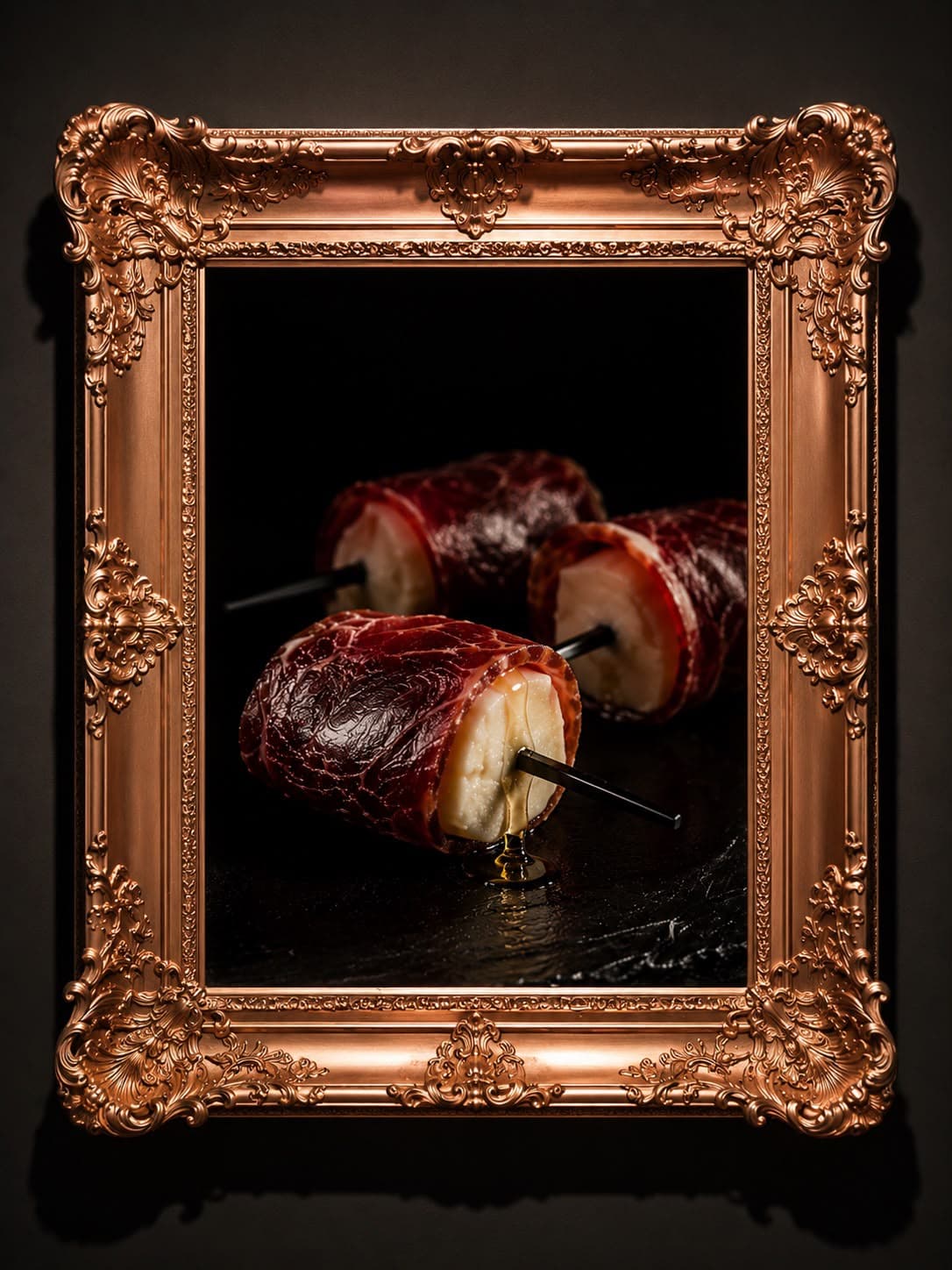 Rulos de jamón ibérico enmarcados en cobre ornamentado sobre pizarra negra húmeda
