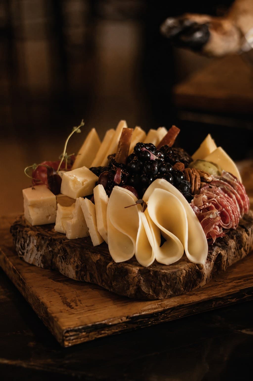 Tabla de quesos artesanos en distintos cortes junto a embutido ibérico y frutos rojos, sobre madera rústica
